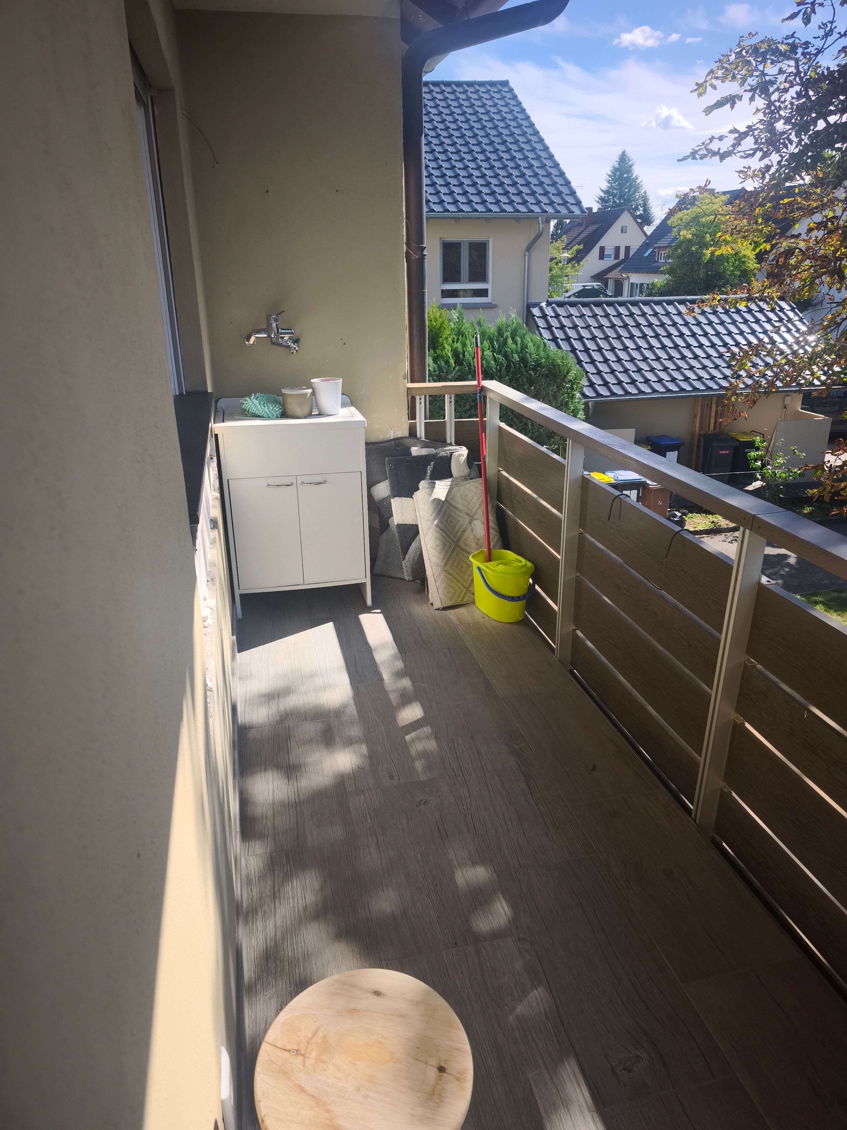 A balcony with a wooden floor, a white cabinet, a yellow bucket, and a red mop.