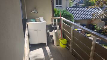 A balcony with a wooden floor, a white cabinet, a yellow bucket, and a red mop.