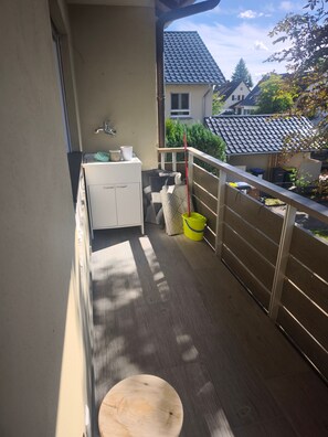 A balcony with a wooden floor, a white cabinet, a yellow bucket, and a red mop.