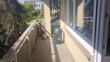 A balcony with a view of the neighborhood, a trash can, and a window.