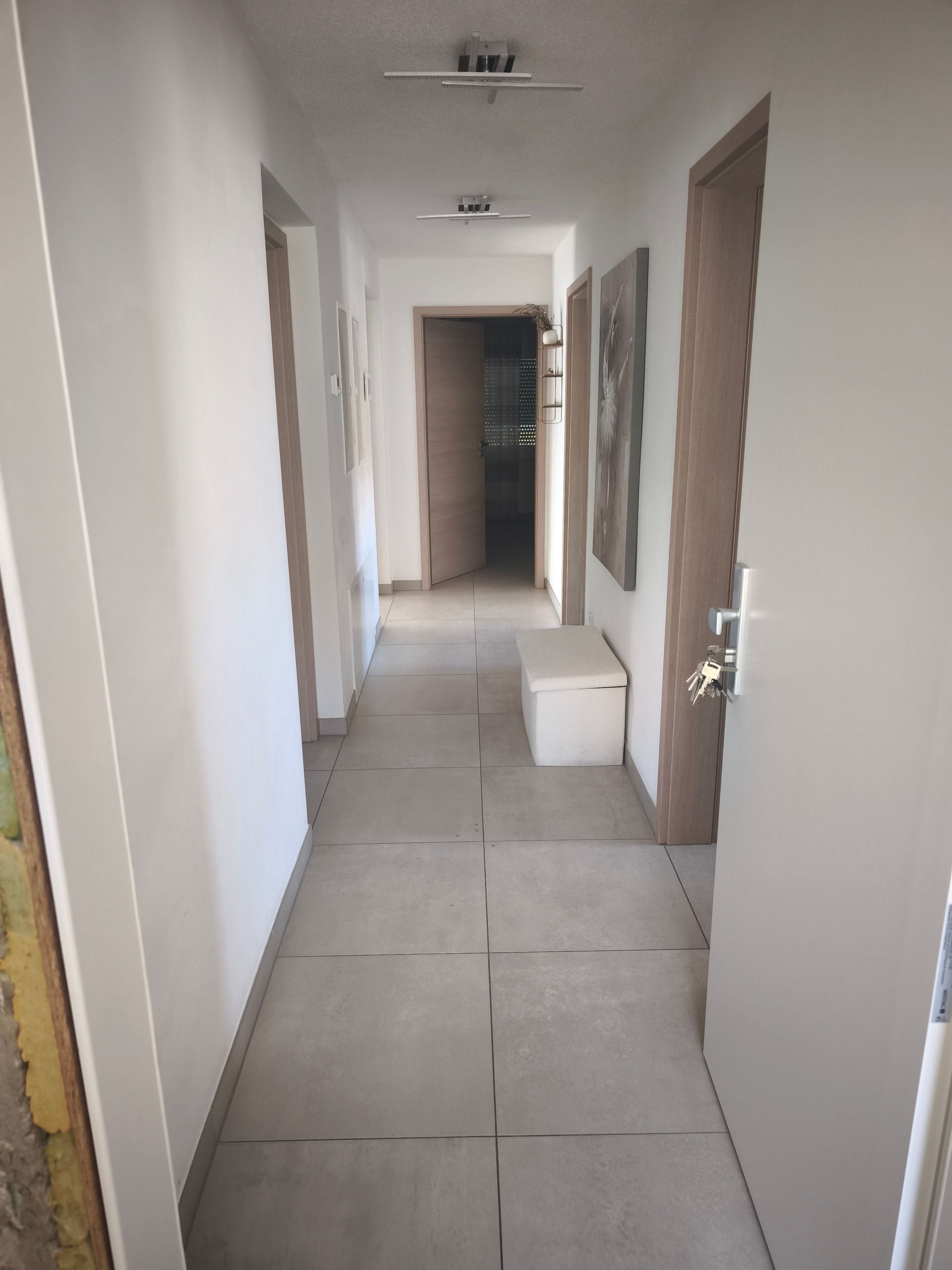 A hallway with a tiled floor, a bench, and a door with a key lock.