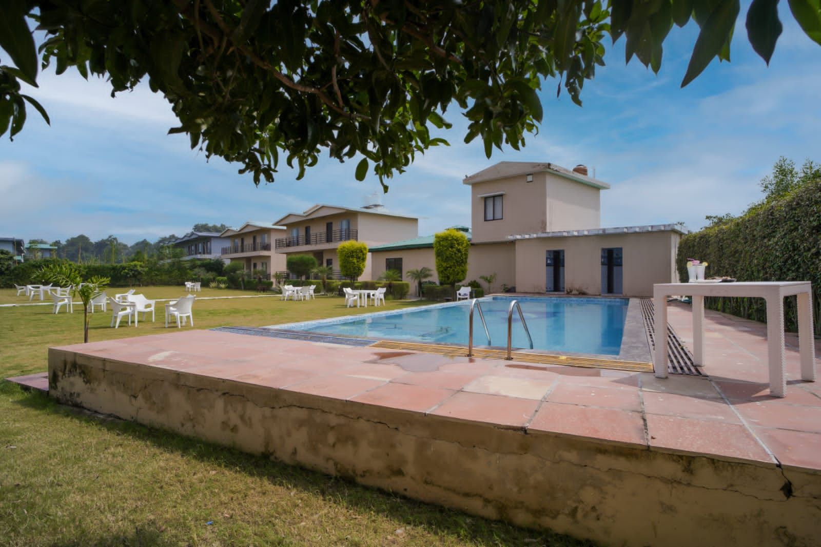 Una piscina con solárium, rodeada de mobiliario exterior y un edificio con varios balcones.