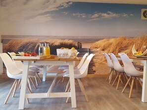 A dining area with a beach view mural, white chairs, a wooden table, and a fruit bowl. - Holiday Home With 5 Bedrooms (Wittmund)