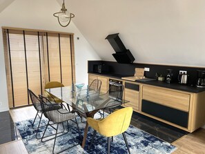 A modern kitchen with a dining area, featuring a glass table, metal chairs, and a black countertop. - Premium Holiday Home, Pink Granite Coast (Perros-Guirec)