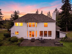 A two-story house with a patio, large windows, and a chimney. - Oak Harbor Retreat • Fire Pit | Mt. Baker + Ocean Views | The Eagle's Nest (Oak Harbor)