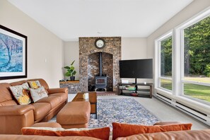 A living room with a fireplace, a sofa, a coffee table, and a television. - Oak Harbor Retreat • Fire Pit | Mt. Baker + Ocean Views | The Eagle's Nest (Oak Harbor)