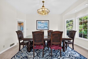 A dining room with a large table, four chairs, a chandelier, and a framed picture on the wall. - Oak Harbor Retreat • Fire Pit | Mt. Baker + Ocean Views | The Eagle's Nest (Oak Harbor)