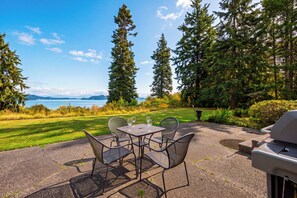 Eine Terrasse im Freien mit Tisch und Stühlen, mit Blick auf ein Gewässer und Berge.