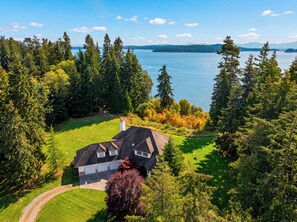 A residential property with a large lawn, a garage, and a view of a lake. - Oak Harbor Retreat • Fire Pit | Mt. Baker + Ocean Views | The Eagle's Nest (Oak Harbor)