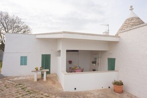 A white building with a small patio area, a table with chairs, and a potted plant. - Trulli in Puglia With Private Forest (Locorotondo)