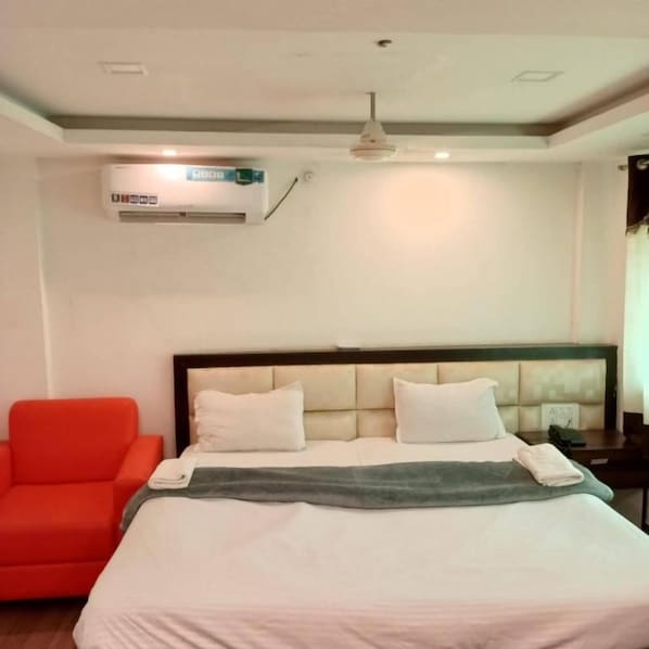 A hotel room with a bed, a red armchair, an air conditioning unit, and a ceiling fan.