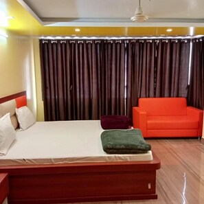 A hotel room with a bed, a red sofa, and a curtain backdrop.