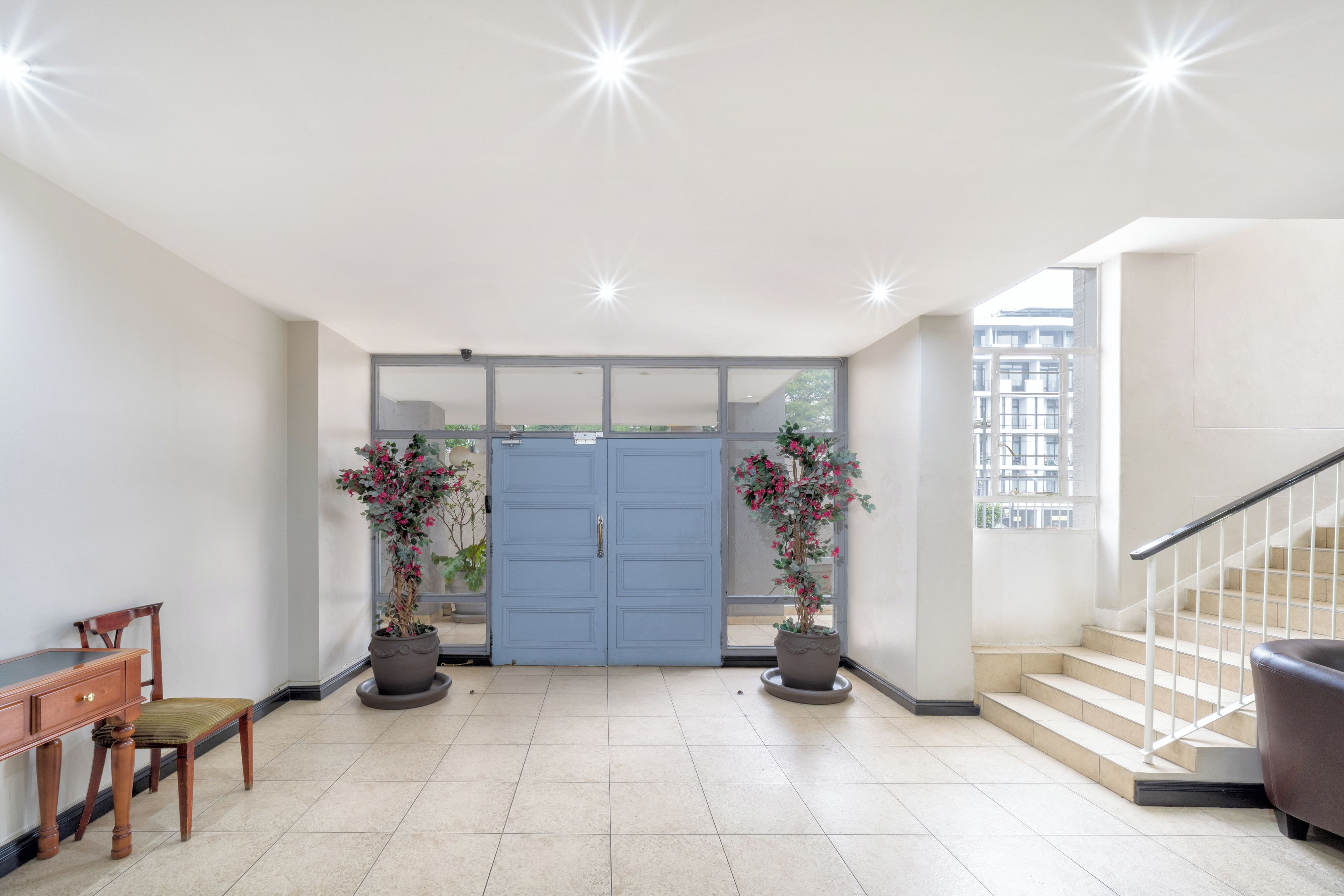 A spacious entrance with a blue door, potted plants, a wooden chair, and a staircase.