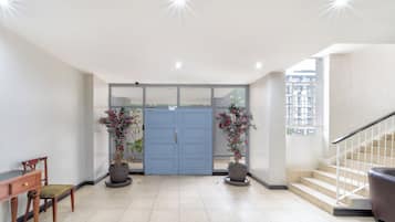 A spacious entrance with a blue door, potted plants, a wooden chair, and a staircase.