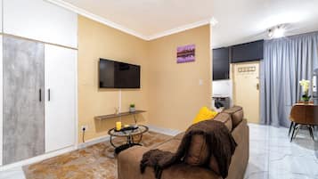 A living room with a sofa, a flat-screen TV mounted on the wall, a small table with a candle, and a decorative item on the wall.