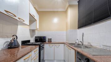 A compact kitchen with white cabinets, a microwave, a kettle, and a dishwasher.