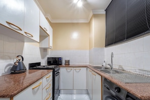Cocina compacta con armarios blancos, microondas, hervidor y lavavajillas.