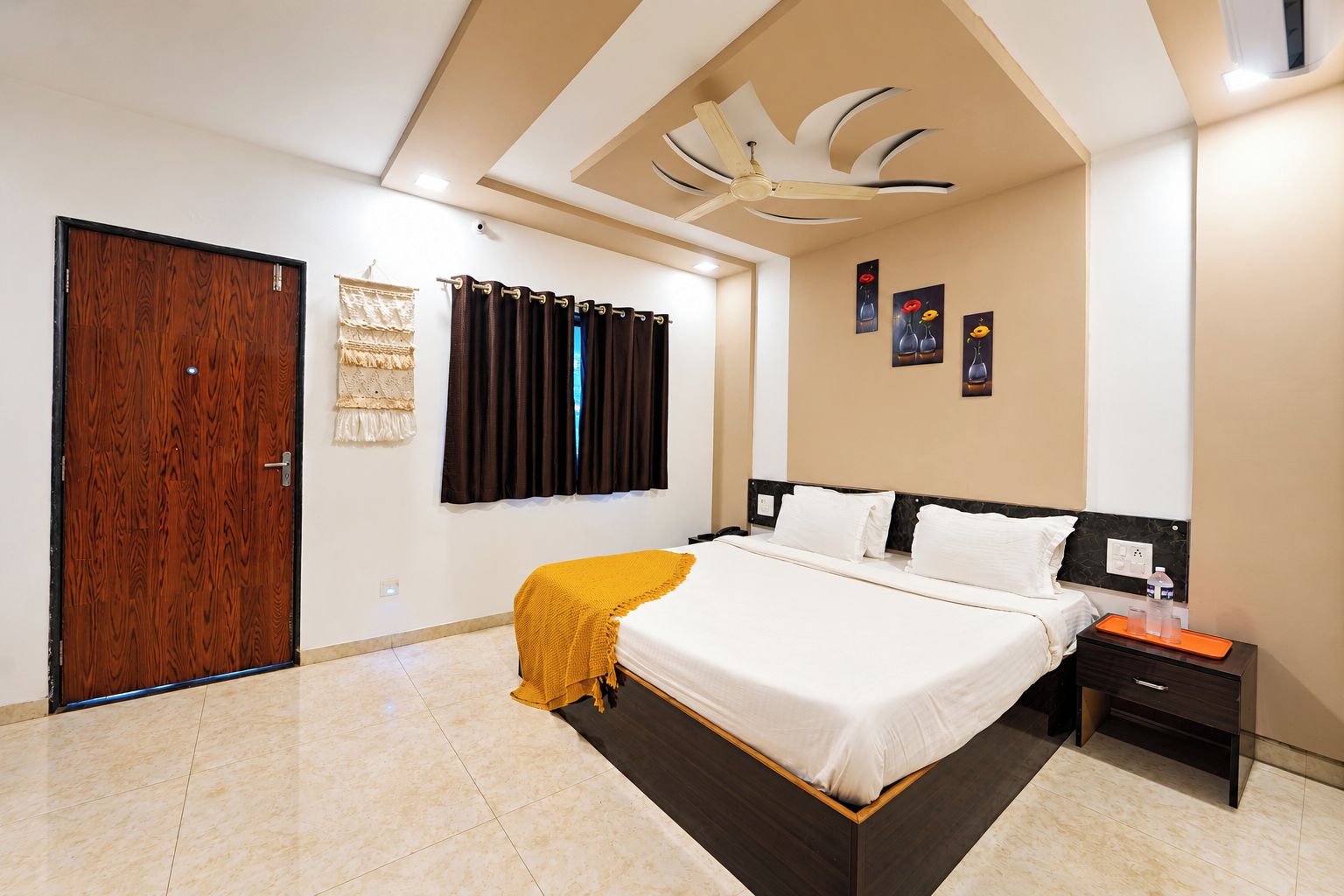 Habitación de hotel con cama, mesita de noche, puerta de madera, ventilador de techo y aire acondicionado instalado en la pared.