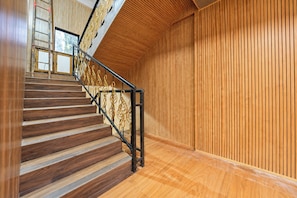 Una escalera de madera con barandilla de metal que conduce a una habitación con paneles de madera verticales.