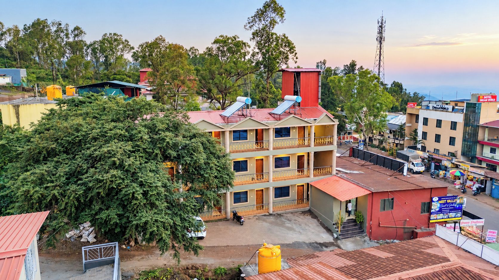 A multi-story hotel with a red roof, balconies, and a large tree in front.
