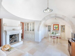 A spacious living room with a fireplace, a dining area, and a kitchen with stone arching. - Trullo in Itria Valley Near Ostuni Beaches (Ostuni)