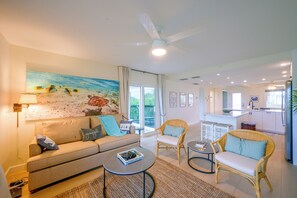 A living room with a sofa, armchairs, a coffee table, and a painting of fish on the wall. - Closest Unit to Beach on Little Gasparilla Island (Placida)
