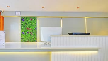 Un mostrador de recepción con una encimera blanca, una planta colgante con flores coloridas y un cartel que indica que no se permite el acceso a visitantes.