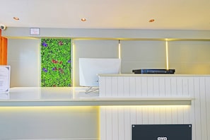 Ein Empfangsschalter mit weißer Theke, eine Wandpflanze mit bunten Blumen und ein Schild, das Besucherrecht freigibt.