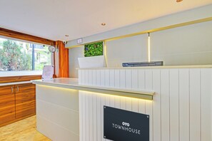 A reception desk with a sign reading 'OYO TOWNHOUSE,' a clock, and a window with a view of greenery. - Super Townhouse CASA GRAND ECIL (Hyderabad)