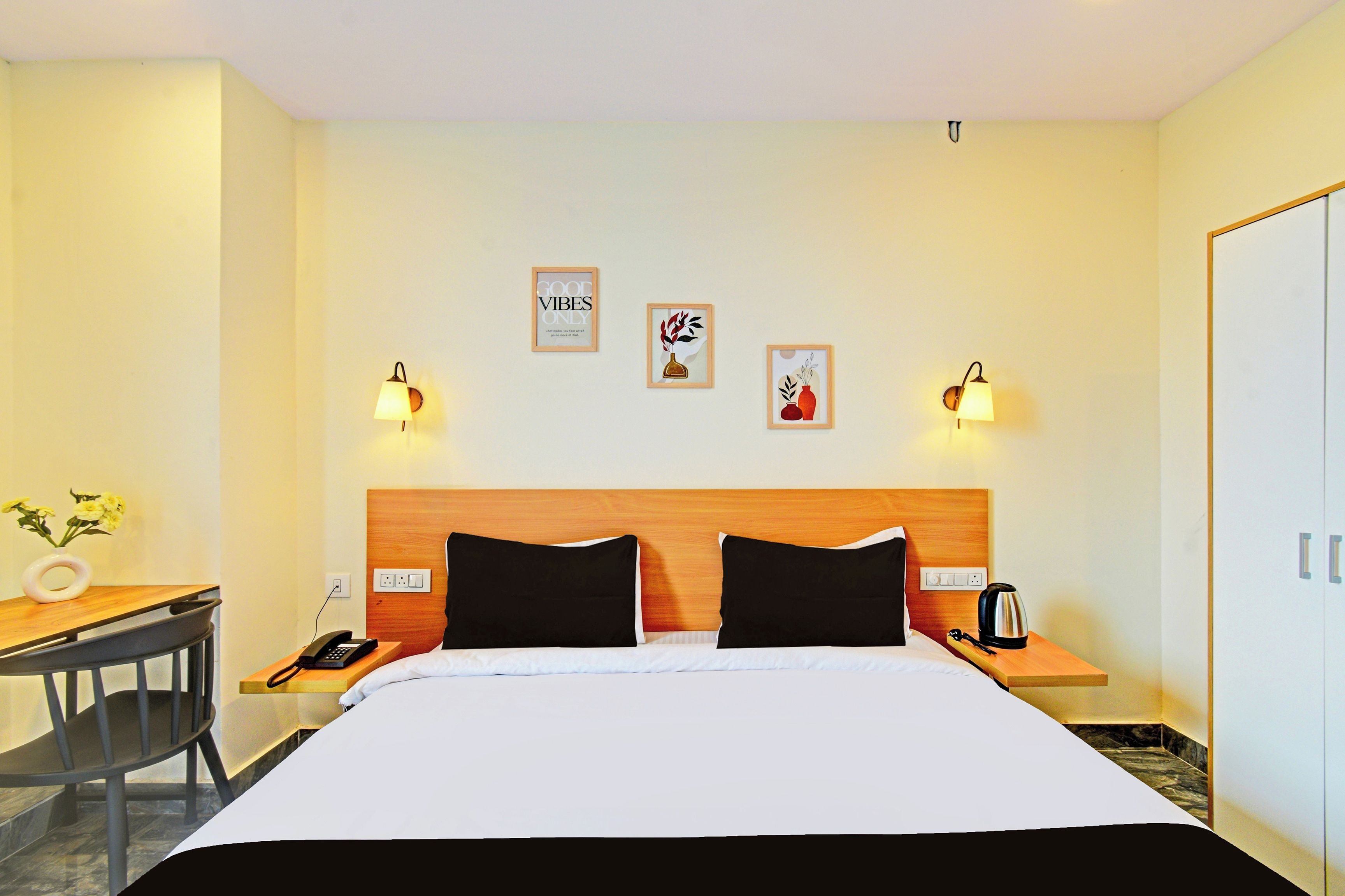 Una habitación de hotel con cama, mesitas de noche, escritorio, silla y cuadros en las paredes.