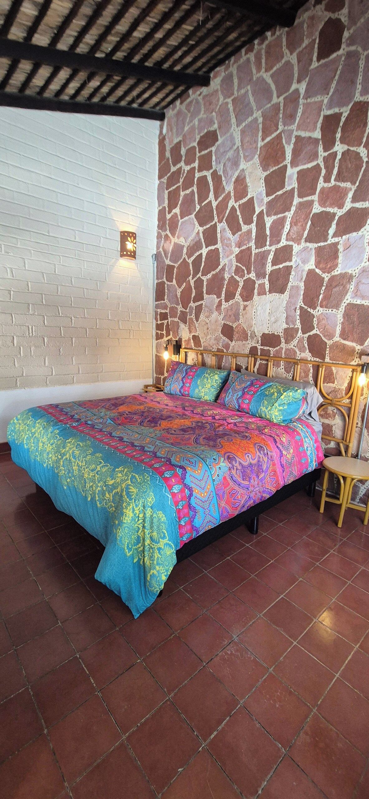 A room with a bed, a chair, a stone wall, and a white brick wall.