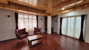 Una habitación amplia con suelo de madera, dos sillones, una mesita y un armario.