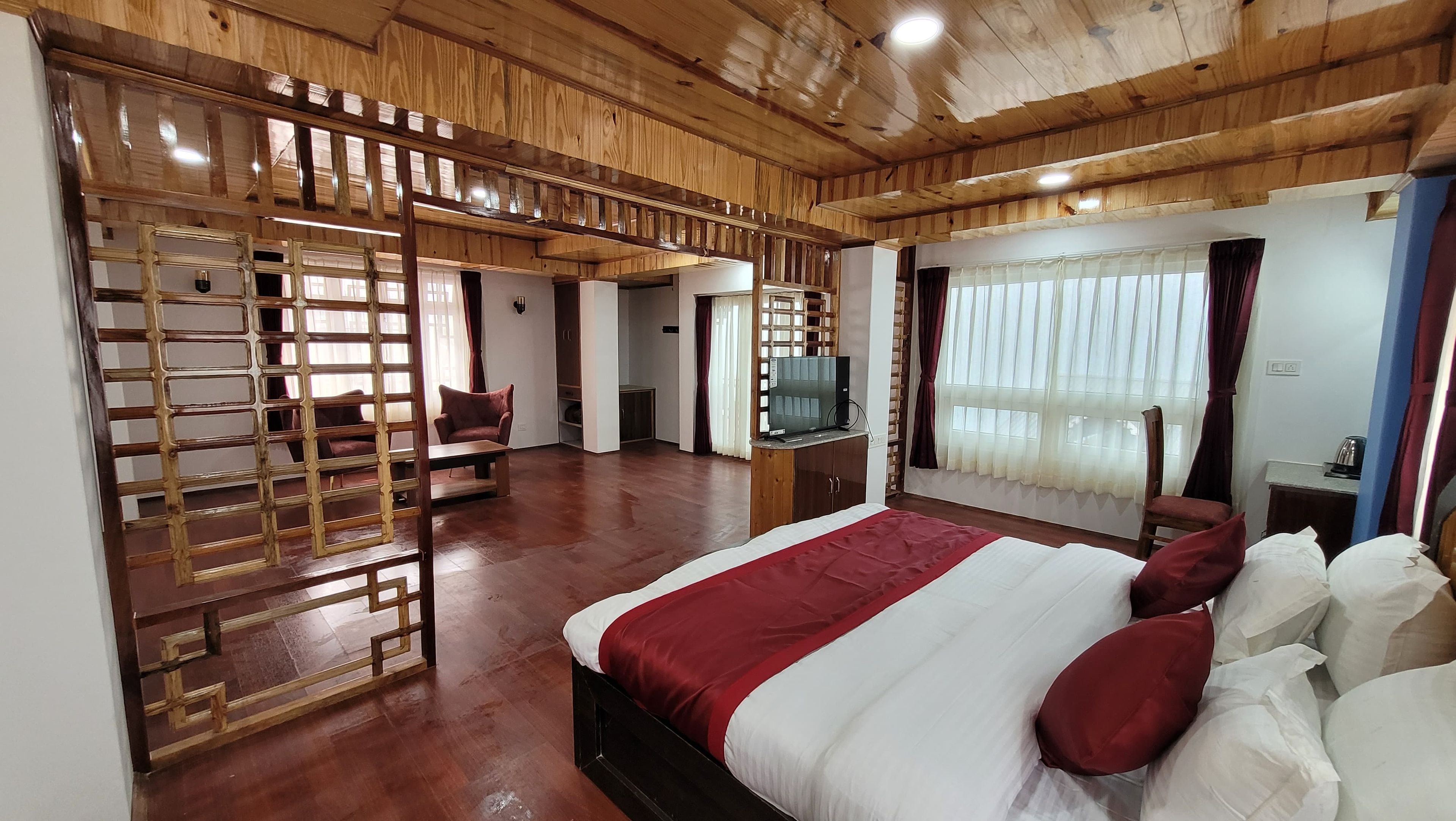 Habitación de hotel con una cama grande, televisión, techo de madera y vistas al exterior.