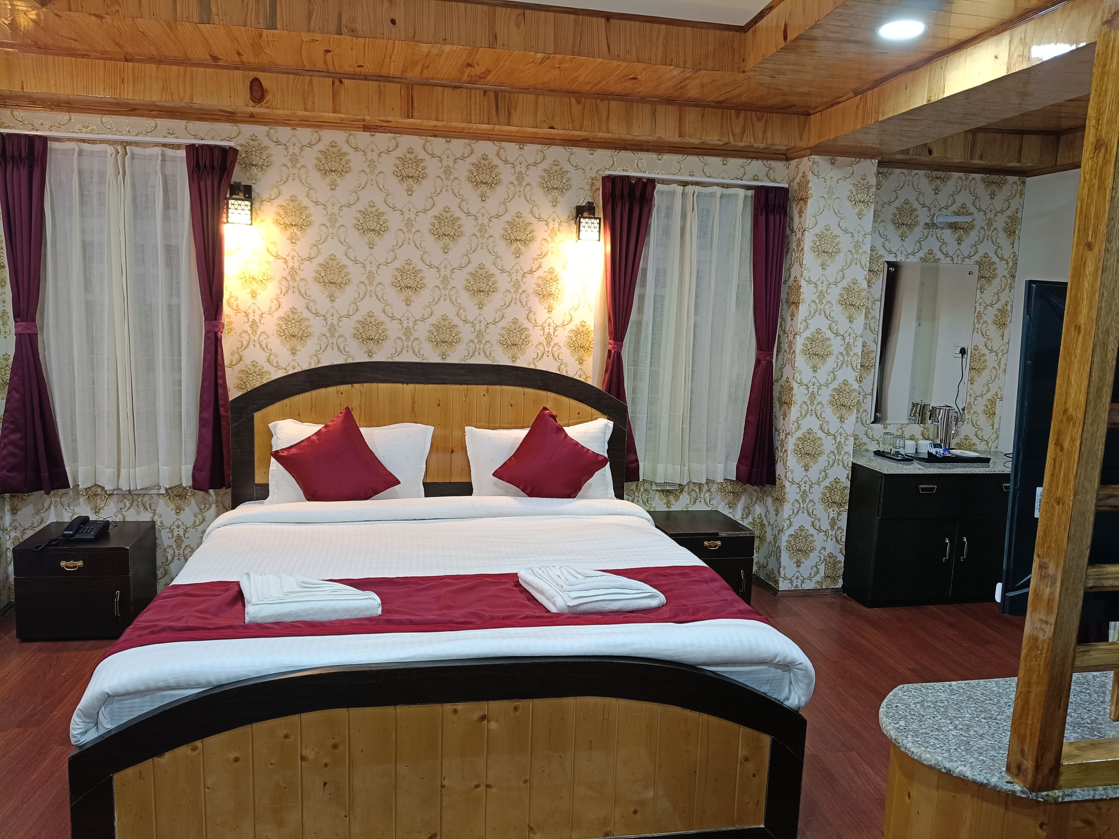 A hotel room with a wooden headboard, a bed with white and red bedding, two nightstands, a mirror, and a vanity with a sink.