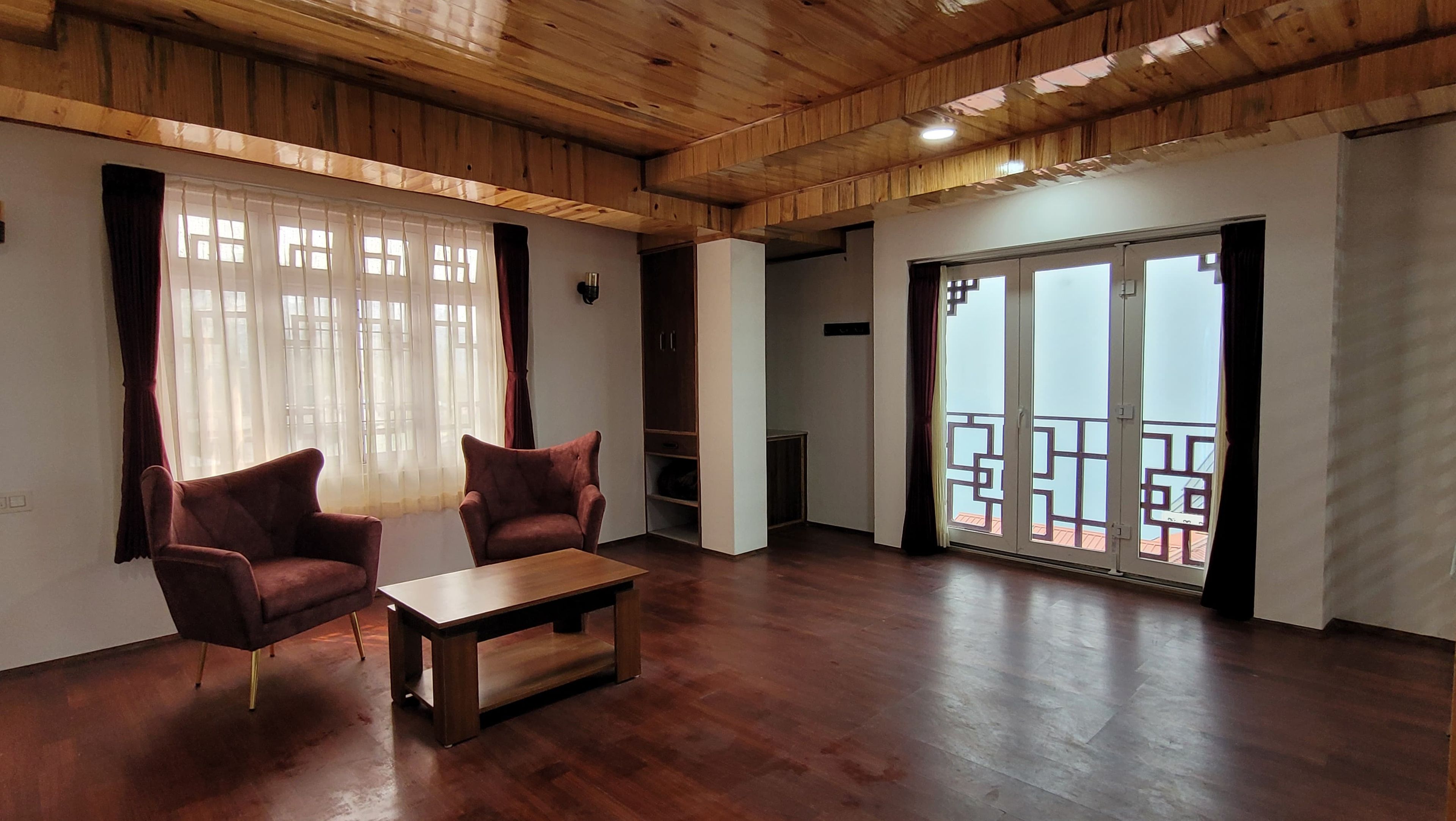 Un salón amplio con techo de madera, dos sillones, una mesa de centro y un ventanal corredero que da a un balcón.