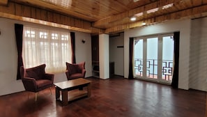 Un salón amplio con techo de madera, dos sillones, una mesa de centro y un ventanal corredero que da a un balcón.