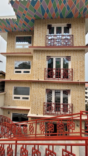 Un edificio de varios pisos con fachada de ladrillo, balcones con barandillas rojas y un toldo colorido con estampado.