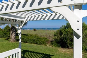 Une pergola blanche offrant une vue sur l’océan et la plage en arrière-plan.