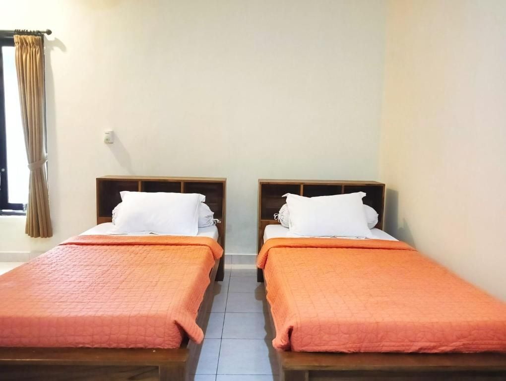 A hotel room with two single beds, each with a wooden headboard and a white pillow. The beds have orange bedding.