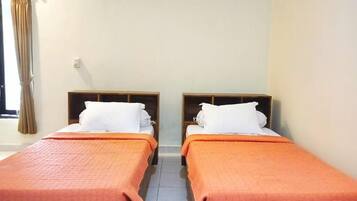 A hotel room with two single beds, each with a wooden headboard and a white pillow. The beds have orange bedding.