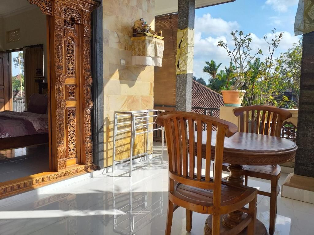 A room with a bed, a wooden chair, a round table, and a balcony with a view of palm trees.