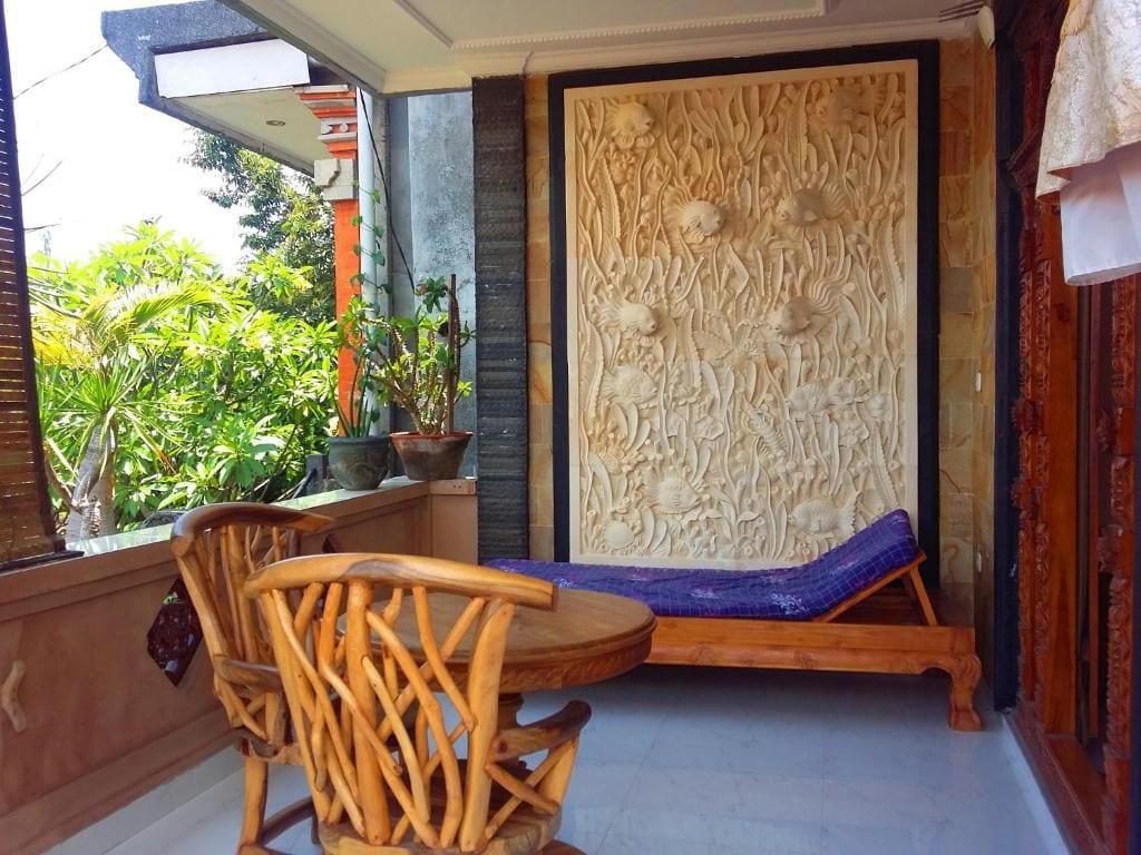 A room with a wooden chair and a bench, a decorative wall panel, and a view of greenery outside.