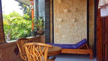 A room with a wooden chair and a bench, a decorative wall panel, and a view of greenery outside.