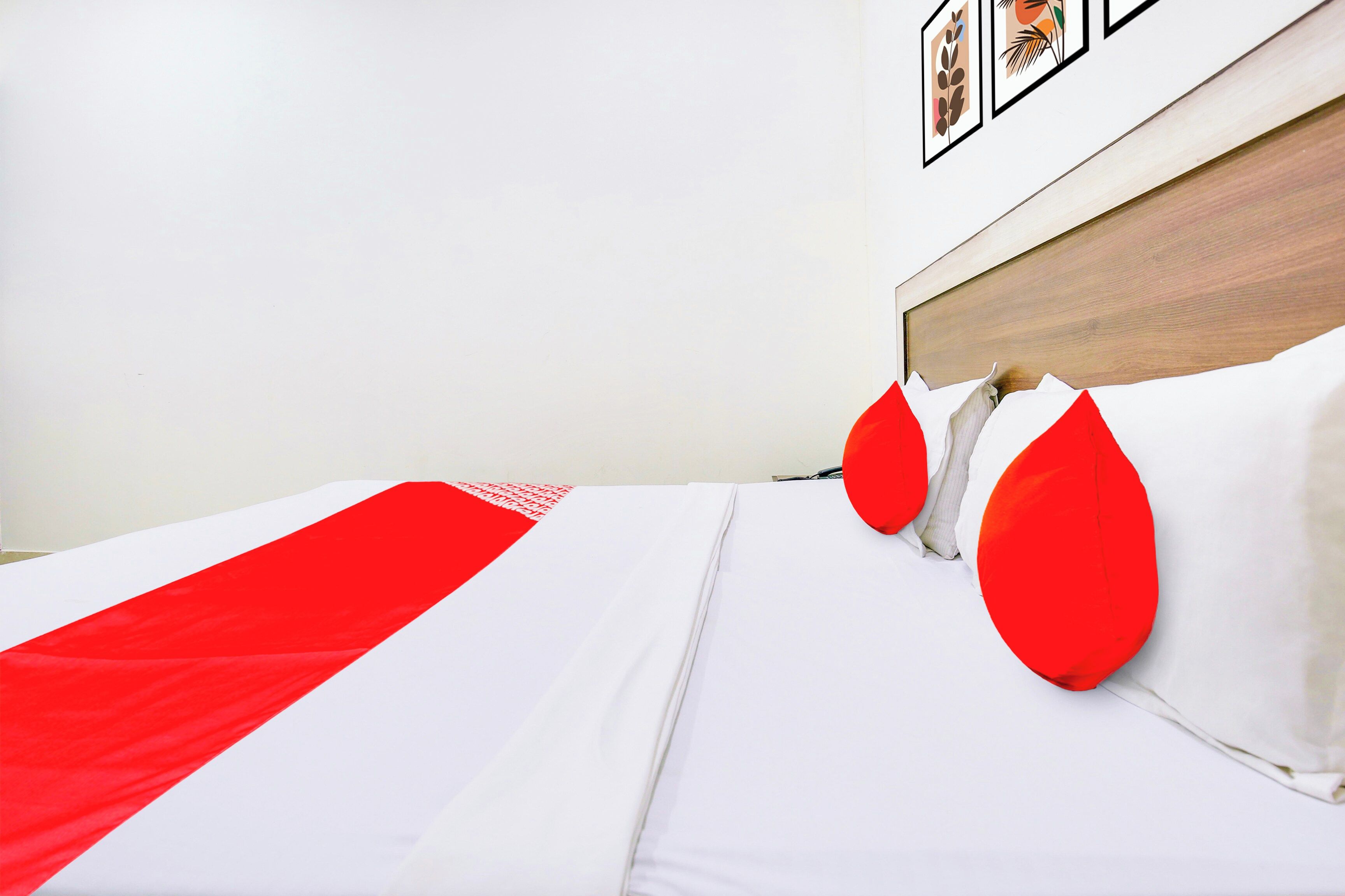 Een net opgemaakt bed met wit en rood beddengoed, een houten hoofdbord en een wand met ingelijste kunstwerken.