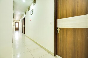 A corridor with a wooden door, white walls, and a tiled floor.