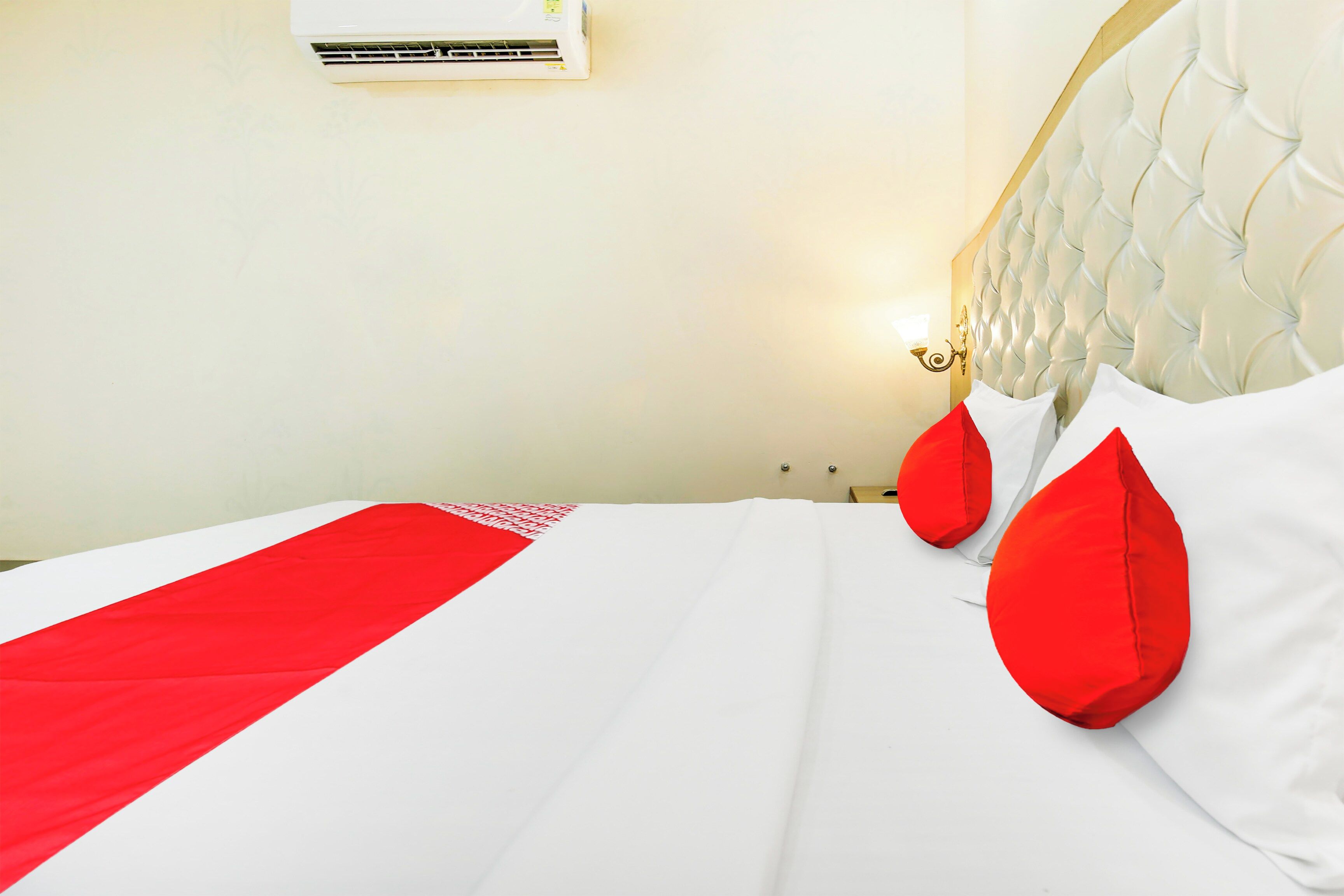 A hotel room with a bed, a wall-mounted air conditioner, and a nightstand with a lamp.