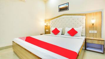 Quarto de hotel com uma cama grande, cabeceira com design acolchoado, duas luminárias de cabeceira e um quadro na parede.
