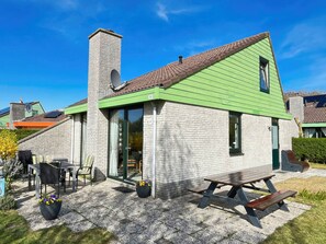 A single-story house with a green roof, a chimney, and a patio area with outdoor furniture. - Holiday Home With 3 Bedrooms (Julianadorp)