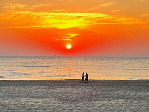 A sunset over the ocean with a ship in the distance and two people standing on the shore. - Holiday Home With 3 Bedrooms (Julianadorp)
