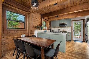A wooden cabin interior with a dining area, kitchen, and a view of the outdoors. - Adventure and Ski All Day, Sip, Soak, and Relax at Night in the Heart of Government Camp (Government Camp)